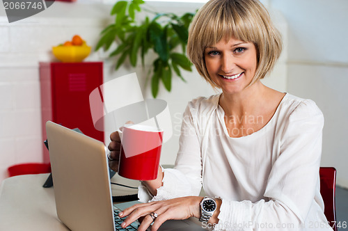 Image of Cheerful woman holding coffee mug and working