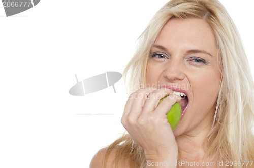 Image of Sexy blonde female eating fresh green apple