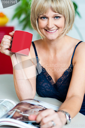 Image of Pretty woman with a coffee mug in hand reading magazine