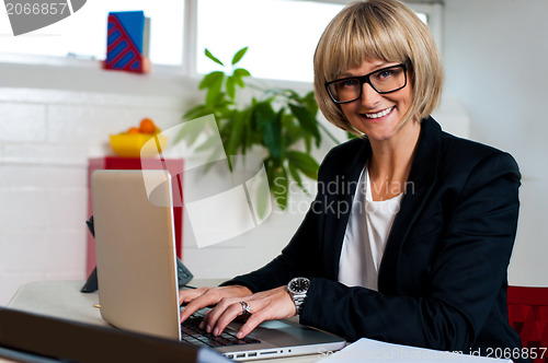 Image of Smiling female manager typing report on laptop