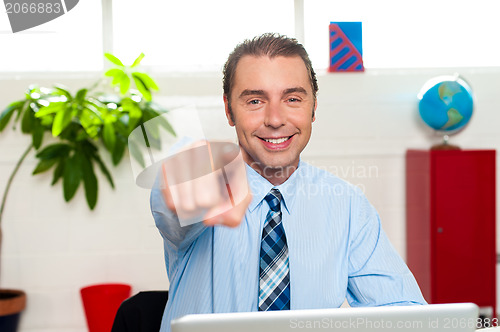 Image of Businessman at work desk pointing at you