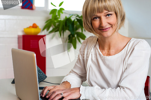 Image of Blonde woman facing camera while working on laptop