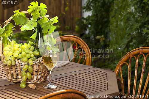Image of White wine bottle and bunch of grapes on basket, glass with in s