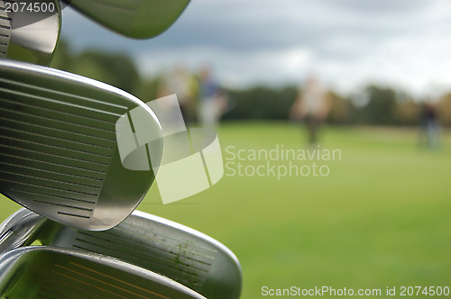 Image of Detail of golf clubs with golfers on the green in the distance