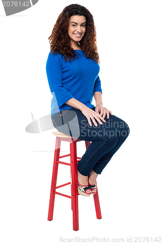 Image of Long curly haired lady seated on red stool