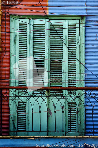 Image of green wood venetian blind and a red blue wall 