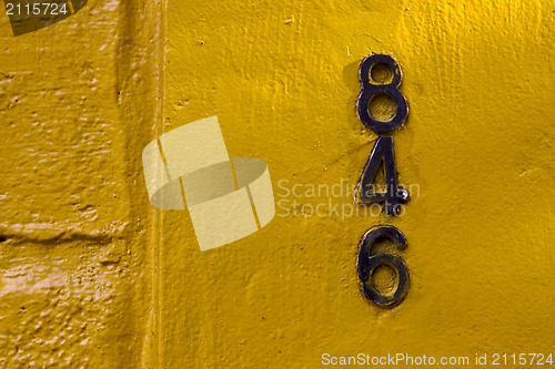 Image of  old black numbers  in a yellow wall 