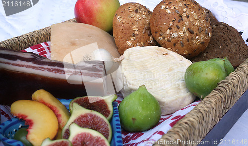 Image of Rustic still life of bread, cheese, bacon and figs in a wicker basket