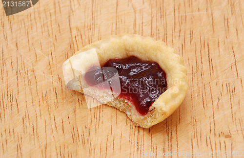 Image of One jam tart with a bite taken, on a wooden table