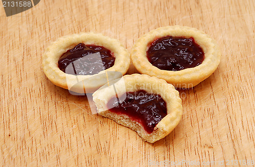 Image of Three jam tarts, one with a bite taken, on a wooden table
