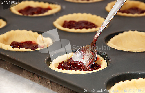 Image of Closeup of jam tarts being filled with a teaspoon