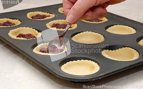 Image of A woman's hand holding a teaspoon as she fills jam tarts