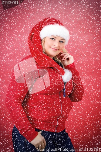 Image of Joyful pretty woman in red santa claus hat smiling with snowflakes