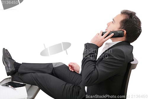 Image of young business man relaxing at office desk and talking on mobile