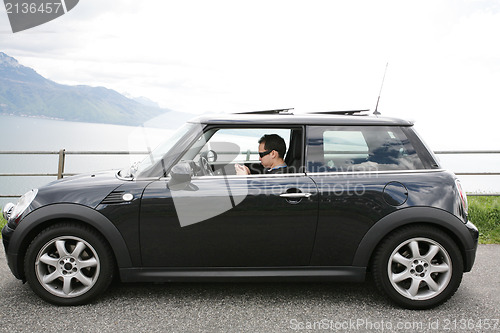 Image of Young man in his fancy car chatting with his device up the hills