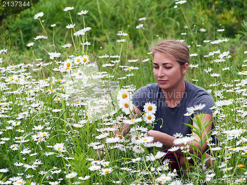 Image of beautiful young woman sitting on a flowering meadow with daisies