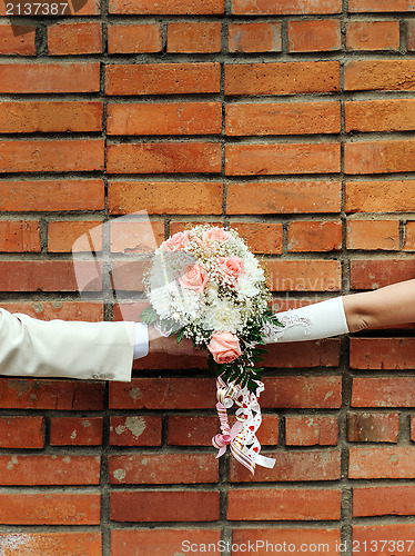 Image of Two hands holding wedding bouquet against a brick wall.