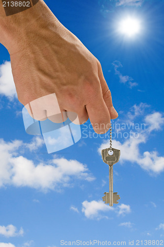 Image of hand holding key on sky background