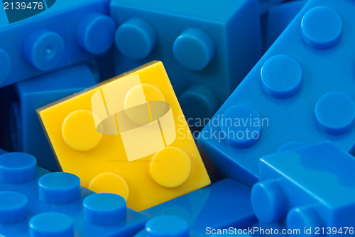 Image of yellow plastic brick in a middle of blue ones