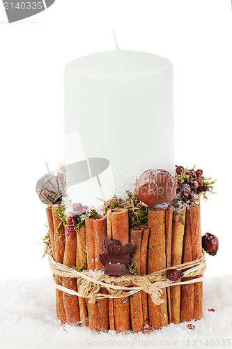 Image of Christmas white candle in a candlestick with cinnamon and dried 