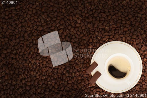 Image of cup of coffee with chocolate pieces on coffee beans background 