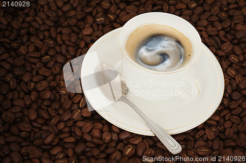 Image of cup of coffee with teaspoon on coffee beans background 