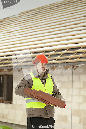 Image of Builder with roof tiles near new building