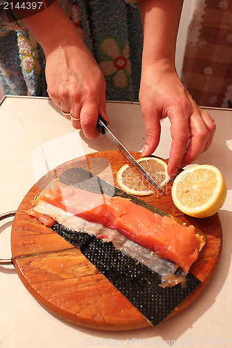 Image of hand cuts slices of a red fish and lemon