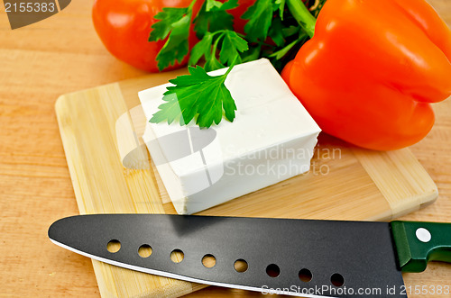 Image of Feta cheese on a board with a knife and vegetables