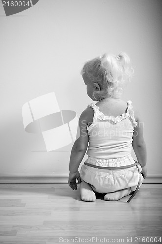 Image of  little girl sits on her knees facing the wall 