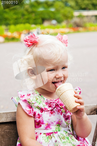 Image of The small blond girl eats ice-cream in a summer garden