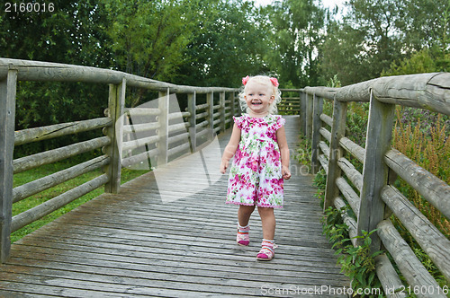 Image of A little girl goes on a wooden bridge