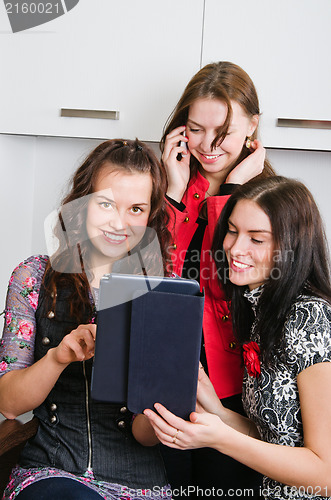 Image of Three women friends chatting at home and using laptop to look at