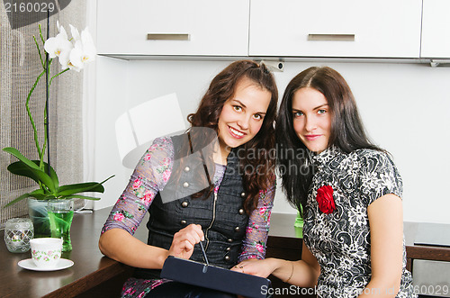 Image of Young women friends chatting at home and using laptop to look at