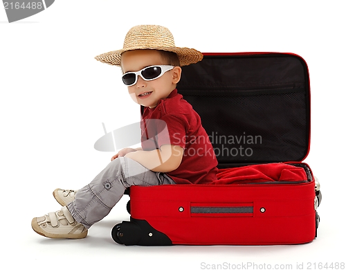 Image of Confident little boy wearing straw hat, sitting in suitcase