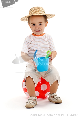 Image of Little boy sitting on dotted ball, holding sandbox toys