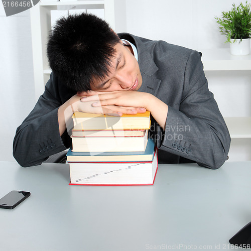 Image of Asian man sleeping on top of a pile of books