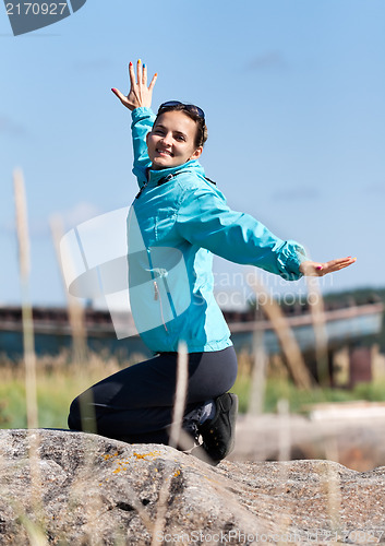 Image of Beautiful girl in a jacket kneeling on a rock