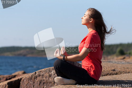 Image of Young girl in lotus pose on the rocks