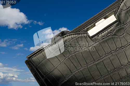 Image of A black business bag on background of sky and clouds