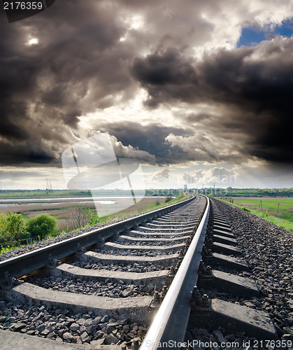 Image of view to railroad goes to horizon under cloudy sky with sun