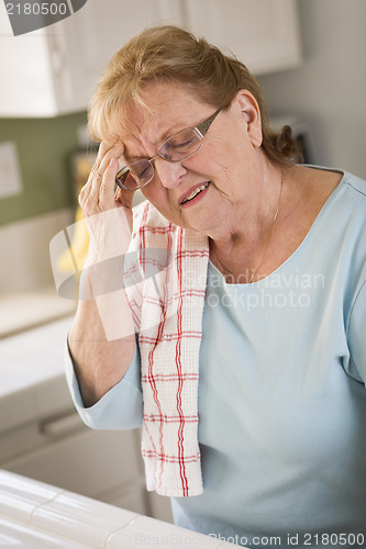 Image of Senior Adult Woman At Kitchen Sink With Head Ache