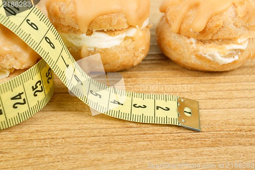 Image of concept of slimming, closeup of caramel cakes with measuring tape