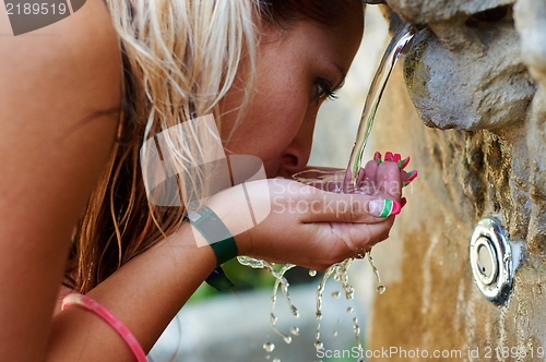 Image of Thirsty girl drinking from outdoor tap