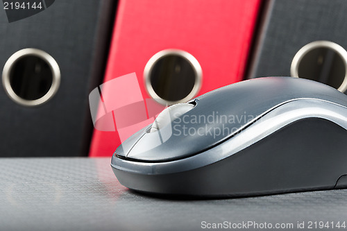 Image of A wireless mouse placed on notebook and three folders in the bac