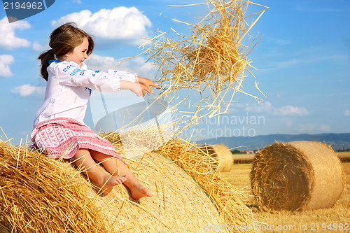 Image of small rural girl on harvest field with straw bales