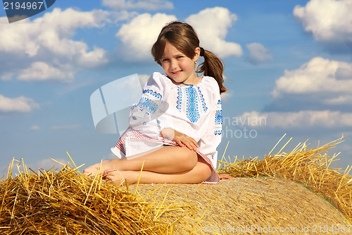 Image of small rural girl on the straw after harvest field with straw bal