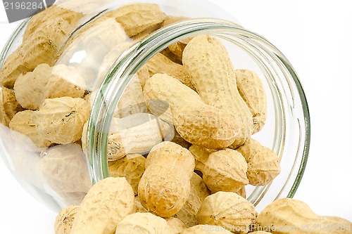 Image of Close up of a glass jar full of unpeeled peanuts on a white back