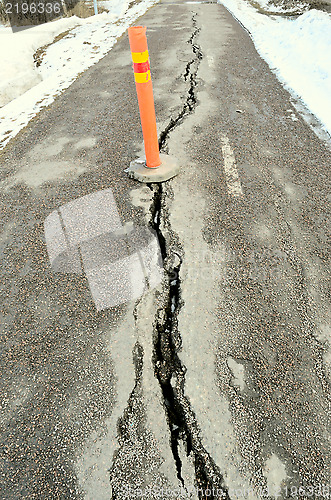 Image of long crack stretching cross the sidewalk  with orange sign