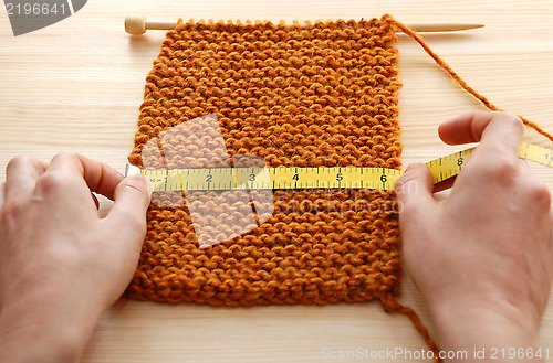 Image of Two hands measuring knitting in inches